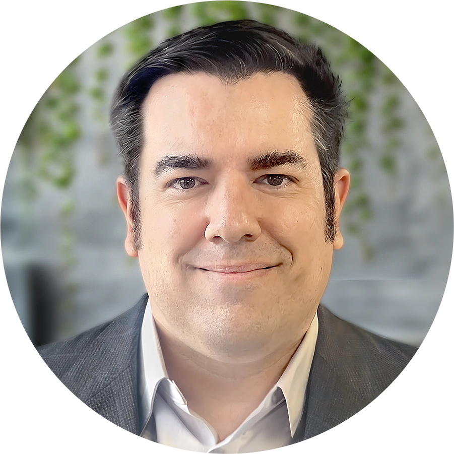 Headshot of Douglas Lambalot, smiling man in a suit with dark hair and sideburns, in front of a plant wall.